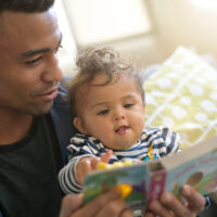 young african-american man reading book story to baby girl